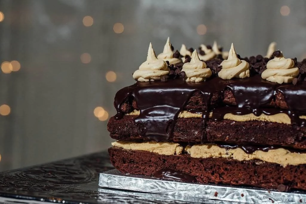 Three-layer chocolate cake with pale filling, glossy chocolate drips and piped peaks
